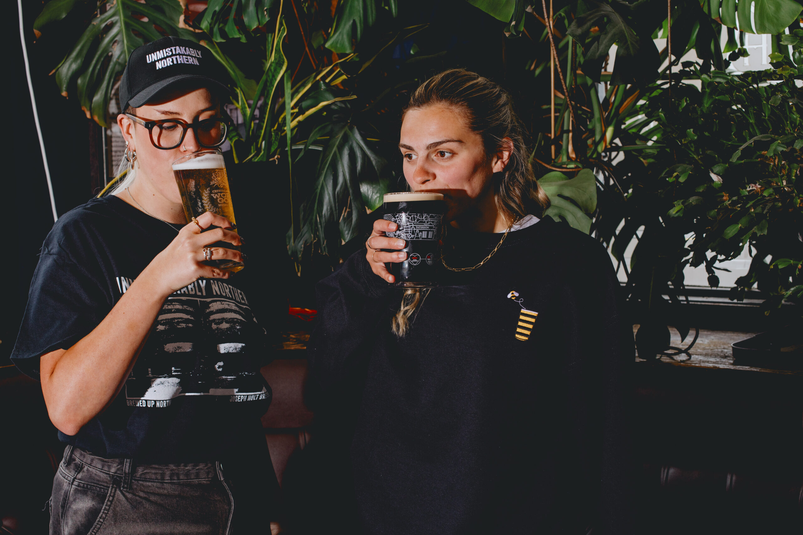 Two girls stood in a pub drinking pints of beer.