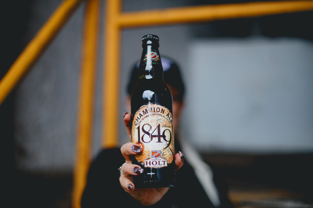 A woman holding an 1849 Champion Ale bottle to the camera.